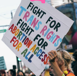 Protester holding a sign that reads " Fight For TRANS RIGHTS FIGHT FOR ABORTION ACCESS FOR ALL.'