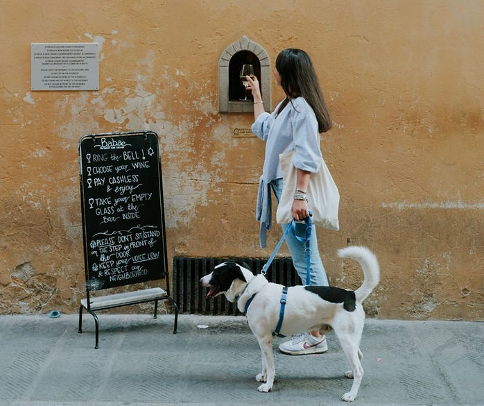Woman with dog buying wine through a historic wine window at Babae Florence