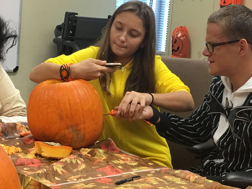 A girl and a boy work together to carve a pumpkin