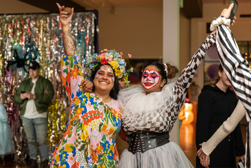 Two women in vibrant costumes, celebrating at an art event