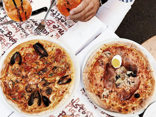 Image of two pizzas on a table next to Aperol Spritz.