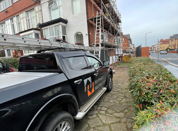Scaffolding, van, ladders on roof, narrow work site.