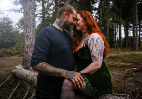 Couple embrace on a log, surrounded by trees.