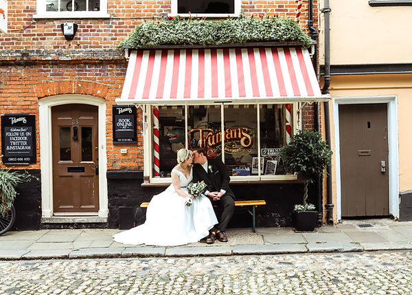 Newlyweds kissing outside a barbershop.