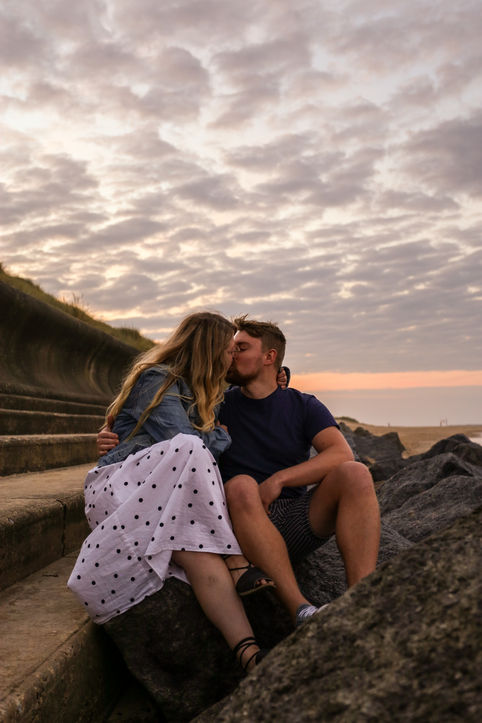 Couple kissing on rocks with clear sky background.
