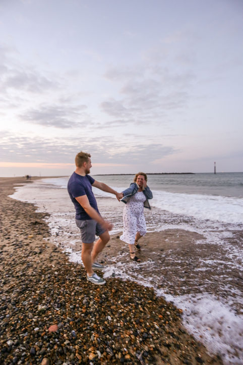Couple holding hands walking along the beach, embracing the waves.