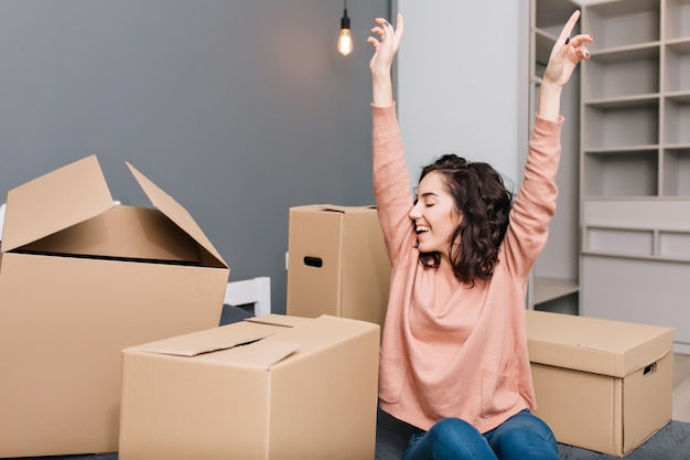 Expressing brightful true emotions, positivity of young pretty woman with short brunette curly hair on bed surround carton boxes in modern apartment. enjoying moving, happiness at new home Free Photo