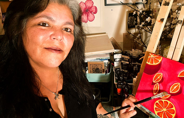 Artist sitting at an easle painting a picture of oranges
