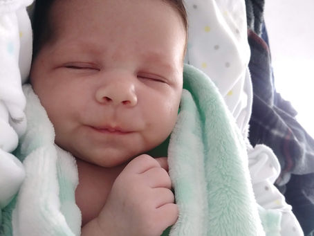 Sleeping baby Aarya wrapped in a mint green blanket, resting peacefully. Soft light, cozy atmosphere, and a hint of a smile on the baby's face.