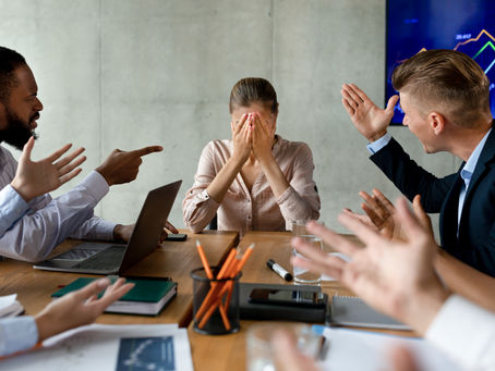 Stressed employee covering face while colleagues argue in a toxic workplace environment