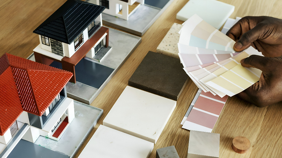 Architect holding color swatches next to miniature house models and material samples for choosing aesthetic room colors.