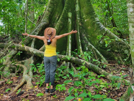 Lorena Saavedra Smith standing before a giant rooted rainforest tree, reflecting on relationship, belonging, and Sumak Kawsay.