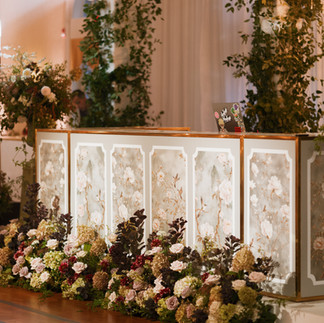 Custom DJ booth featuring a floral-patterned front, lush ground florals, and greenery accents designed for an elegant reception space.