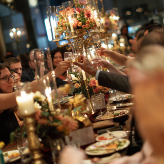 Guests raising glasses around a candlelit table featuring a floral candelabra centerpiece during an elegant celebration.