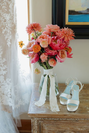 Custom bridal bouquet designed by Philadelphia Event Decor featuring lush coral, peach, blush, and cream flowers displayed alongside the bride's wedding shoes before an Oregon wedding ceremony.