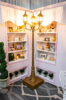Custom boutique display shelving fabricated and installed by Bobby Morganstein Events, featuring built-in shelving, curated decorative props, elegant lighting, and Parisian-inspired details that create a charming café storefront setting.