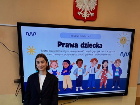 Adwokat Natalia Lech w klasie obok tablicy interaktywnej z prezentacją o prawach dziecka. Prezentacja zawiera tytuł „Prawa dziecka” i ilustracje dzieci.