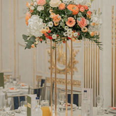 Close up of a tall peach and white floral display on a slim gold stand at a wedding reception