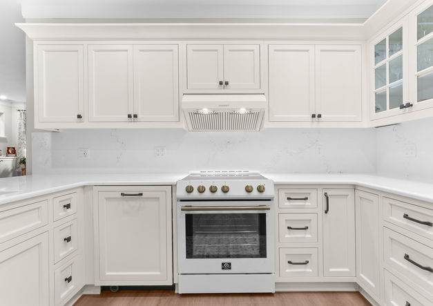 Complete kitchen remodel in a bungalow-style home featuring cream cabinets, white appliances, quartz countertop with matching solid backsplash, new flooring and baseboards, updated lighting, and fresh paint.