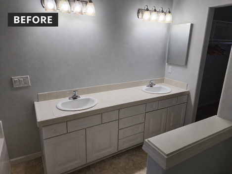 Bathroom before remodeling with a long double-sink vanity, white cabinetry, tiled countertop and small wall mirrors.