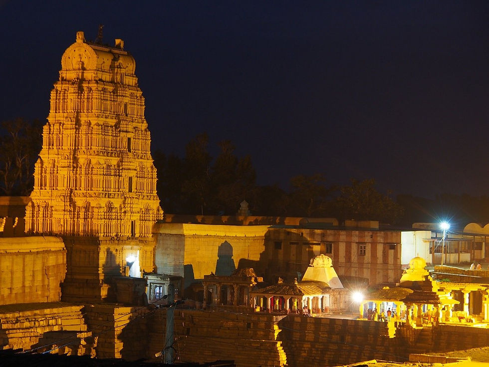 Illuminated Hindu temple complex at night, with a tall golden gopuram against a dark sky and glowing courtyard lights