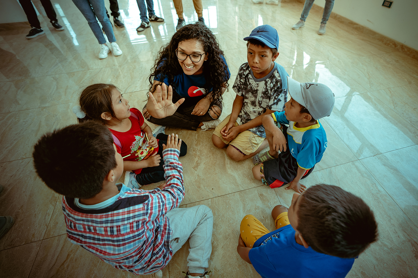 kids sitting in a circle on the floor, one kid is giving a high five to a volunteer