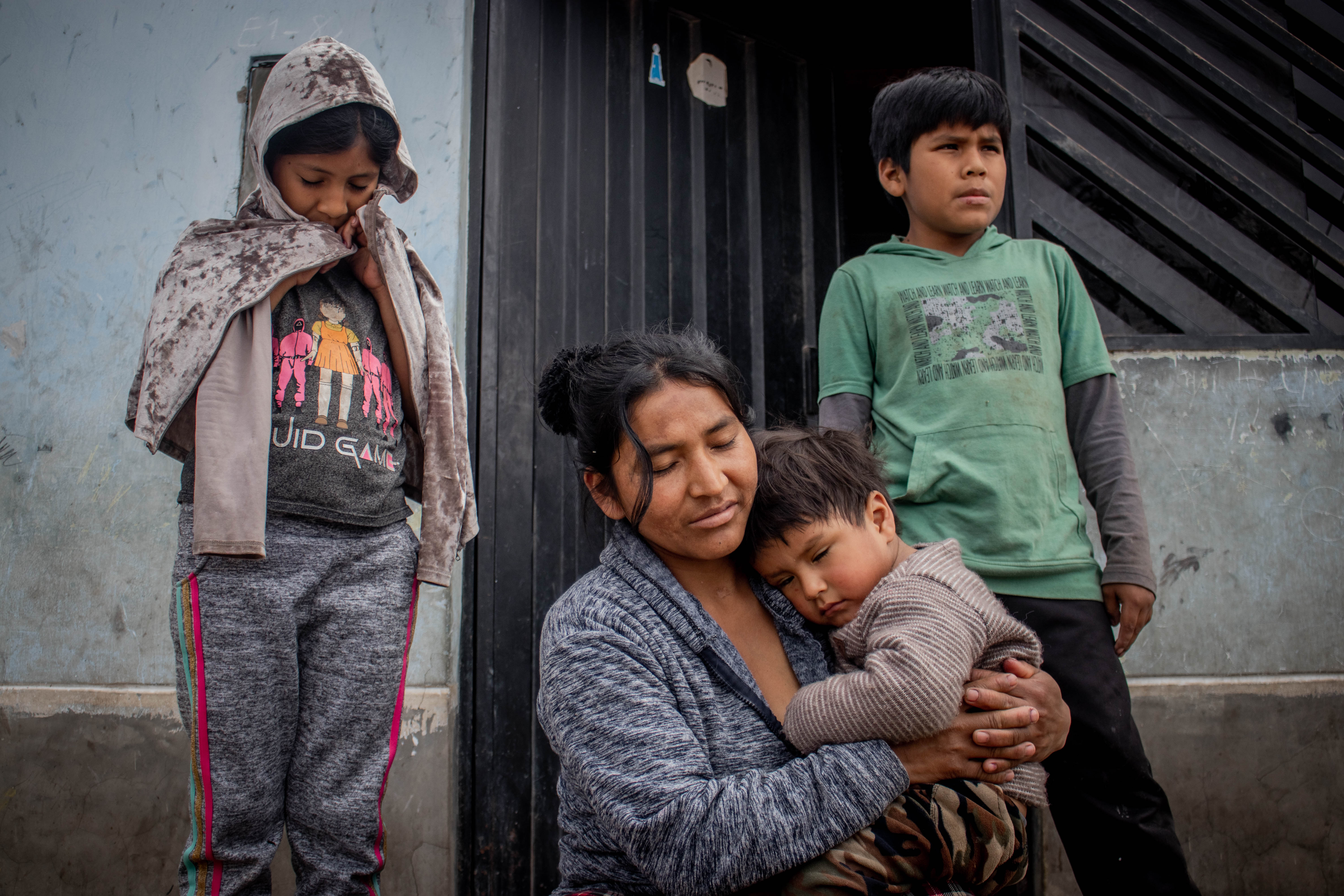 mother holding her young son and her two kids standing behind her
