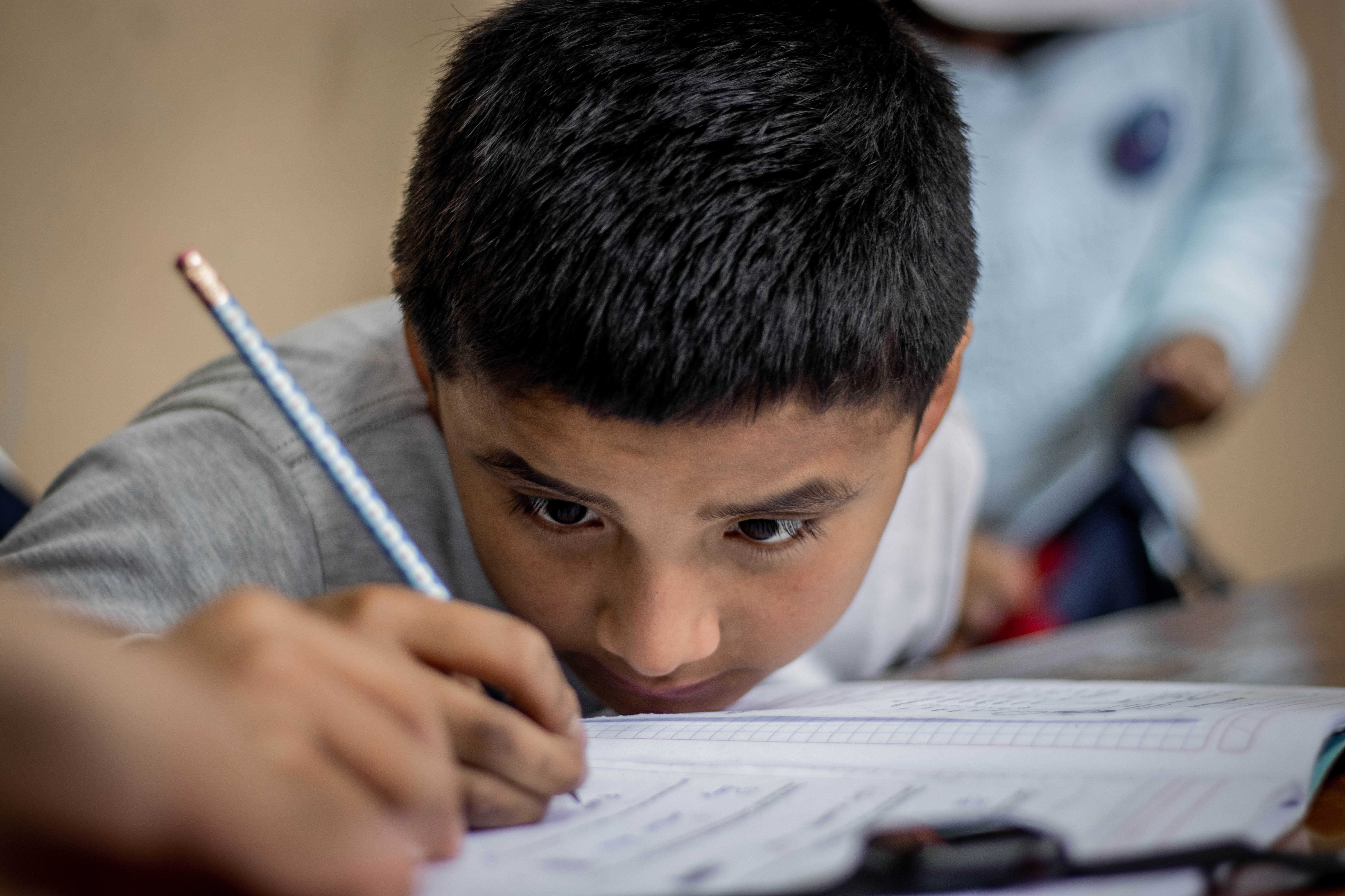 young boy writing on a work book with a pencil