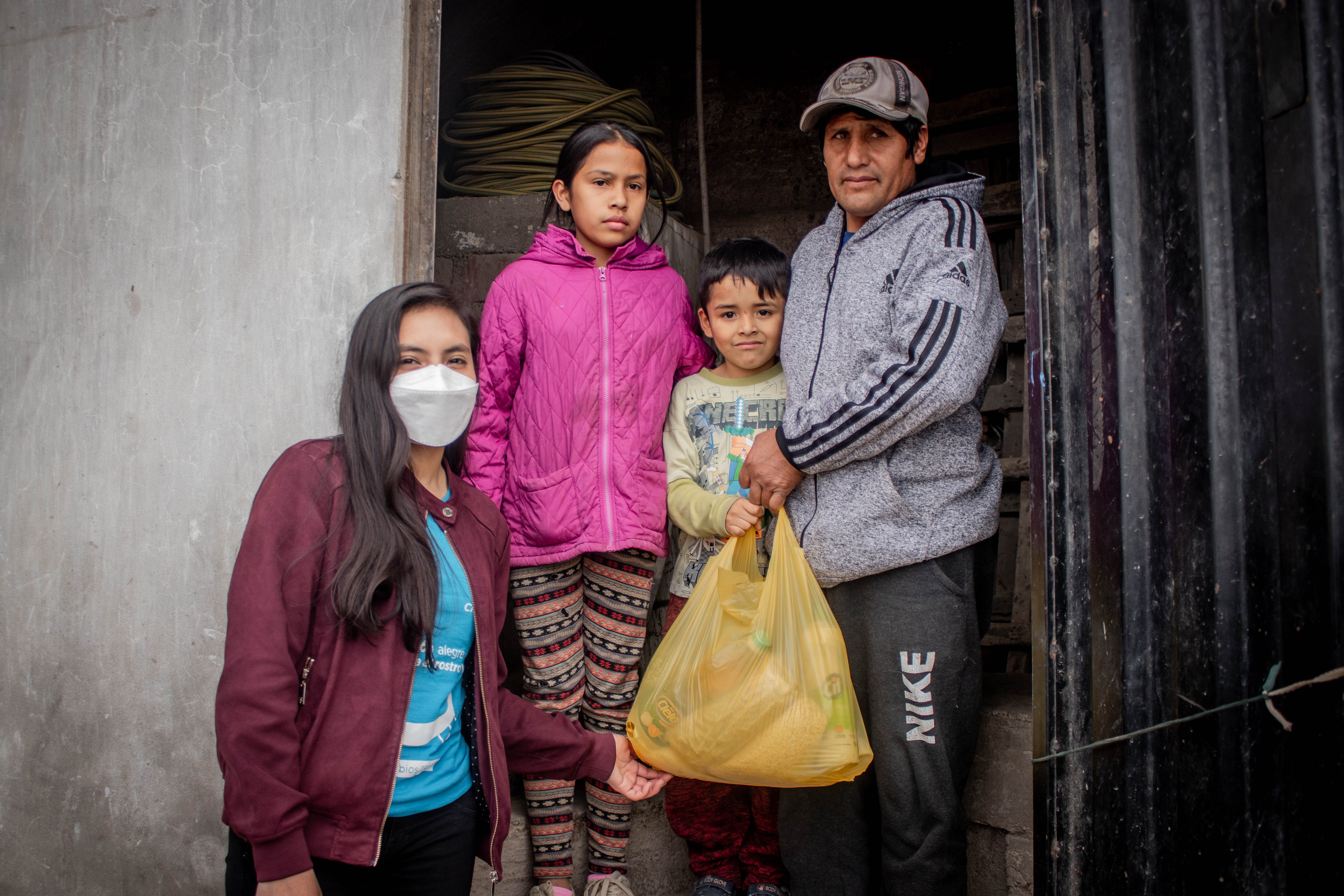 Family standing in front of their house holding a yellow plastic bag