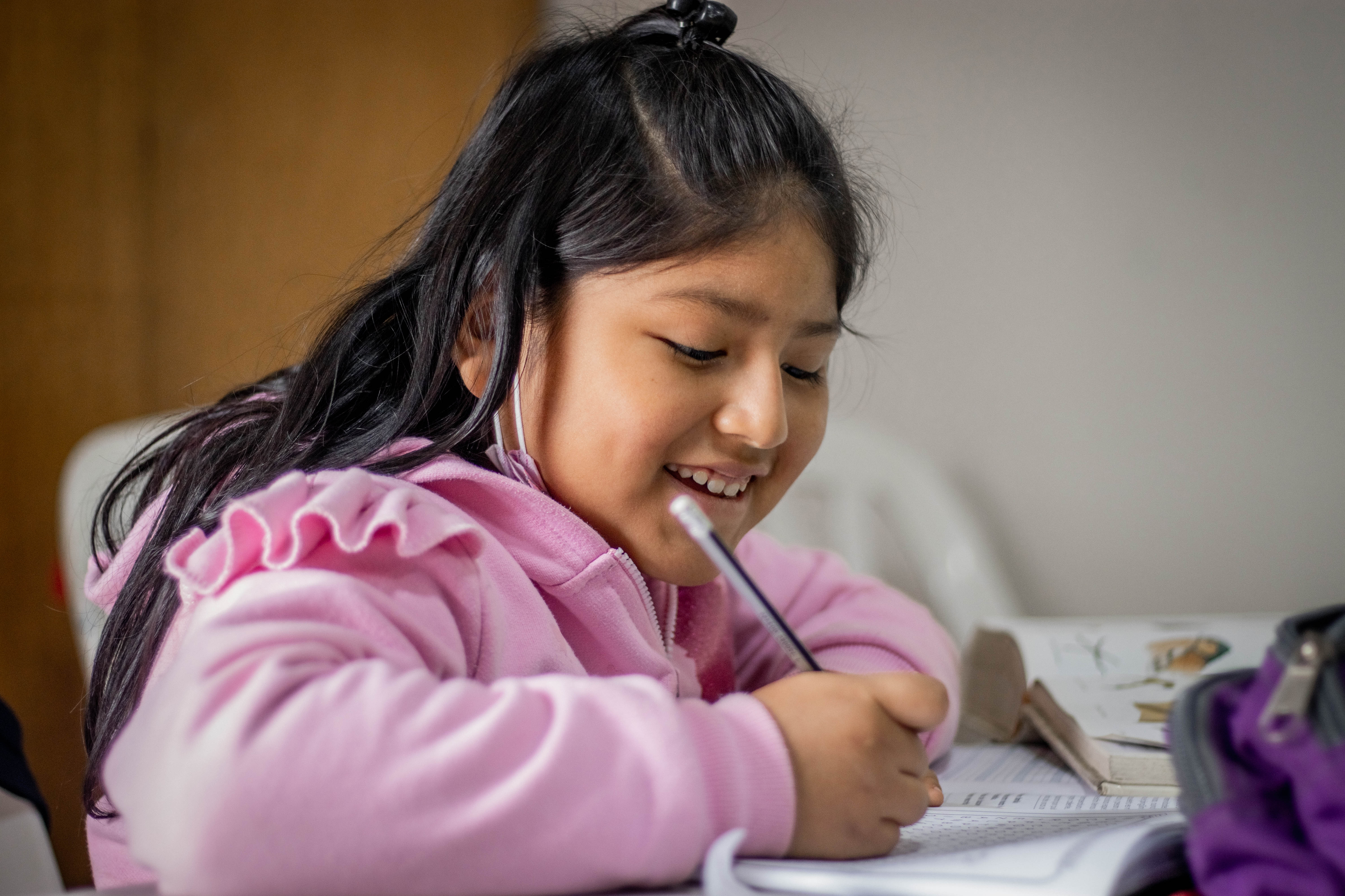 young girl in pink hoodie writing with a pencil