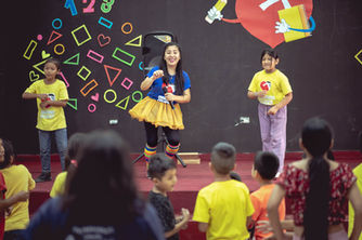 a volunteer and students up on stage leading the rest of the kids in a dance