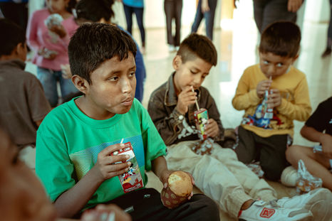 three young boys sitting on the floor drinking juice boxes
