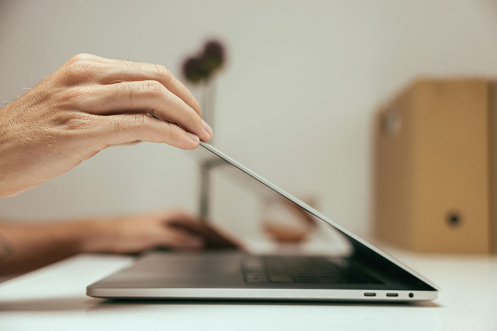 Hand closing a laptop on a white desk, with a blurred beige background, creating a serene and focused atmosphere.