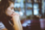 Young woman with closed eyes and clasped hands in a prayerful pose. Blurred indoor background, soft lighting, contemplative mood.