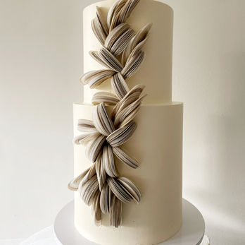 Een 2-laagse bruidstaart met een verhoogde onderste laag. Afgewerkt in een gebroken witte botercrème. Versierd met wafer paper in diverse tinten beige, zand en taupe. Door ze te mengen geeft het een gemêleerd effect.
Nijverdal, Nederland, Overijssel, moderne bruidstaarten, bruiloft, sweet table, Mykitchenplayground