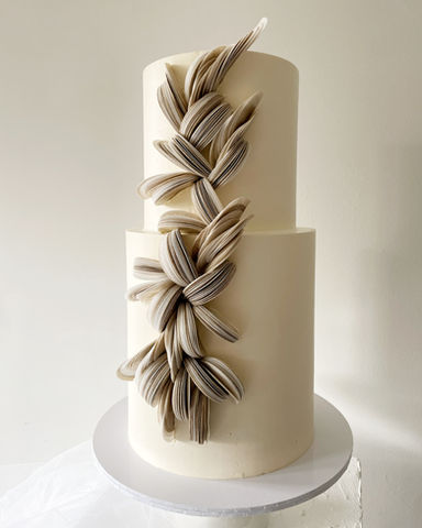 Een 2-laagse bruidstaart met een verhoogde onderste laag. Afgewerkt in een gebroken witte botercrème. Versierd met wafer paper in diverse tinten beige, zand en taupe. Door ze te mengen geeft het een gemêleerd effect.
Nijverdal, Nederland, Overijssel, moderne bruidstaarten, bruiloft, sweet table, Mykitchenplayground