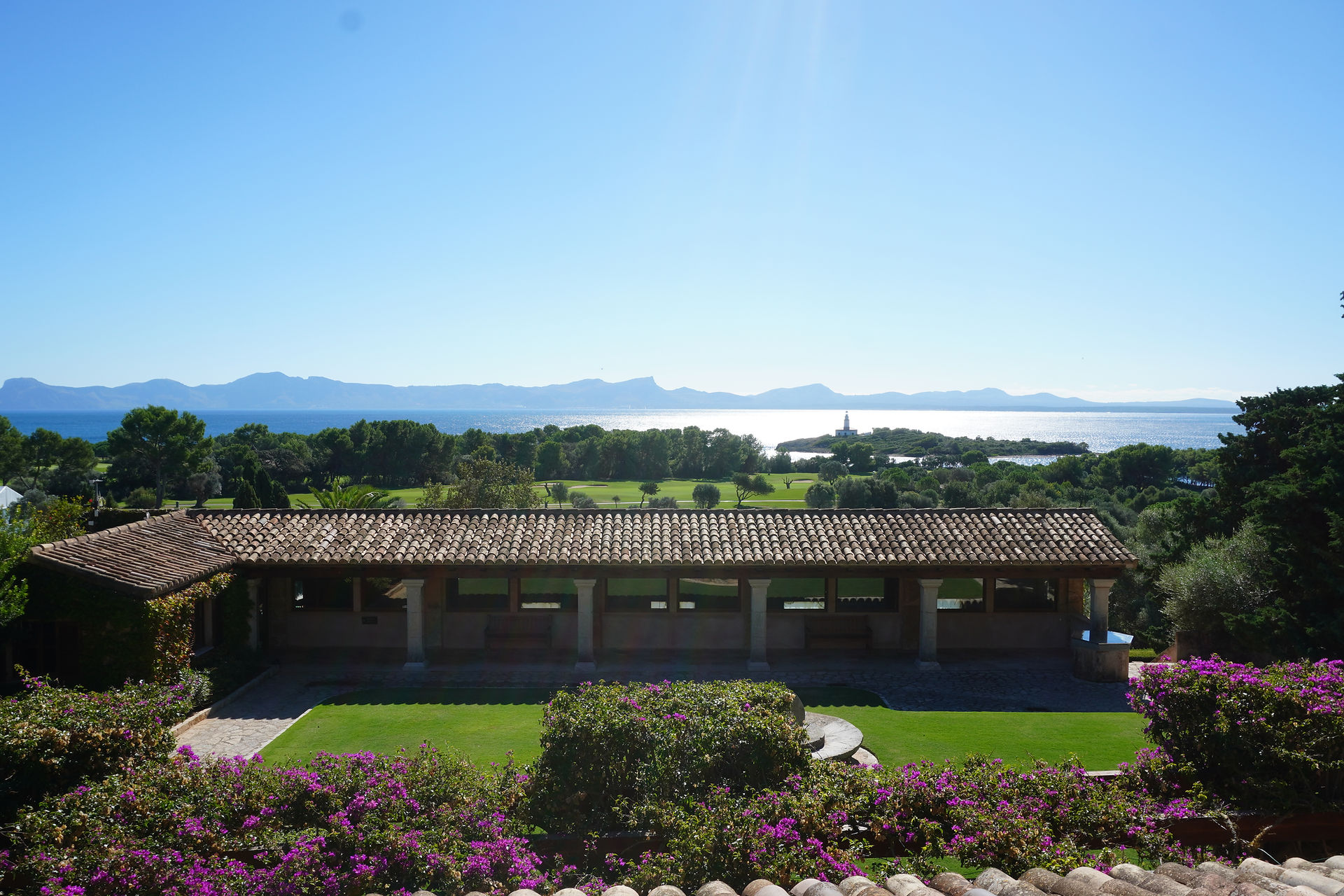 Udsigt fra Club de Golf Alcanada over golfbanen, Middelhavet og bjergene på Mallorca med blomster.