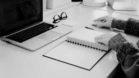 Person using a laptop at a desk, and touching a paper notebook. Image courtesy of https://unsplash.com/@stilclassics