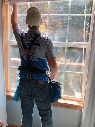 Residential window cleaning technician cleaning exterior home windows with squeegee in Three Rivers MI.