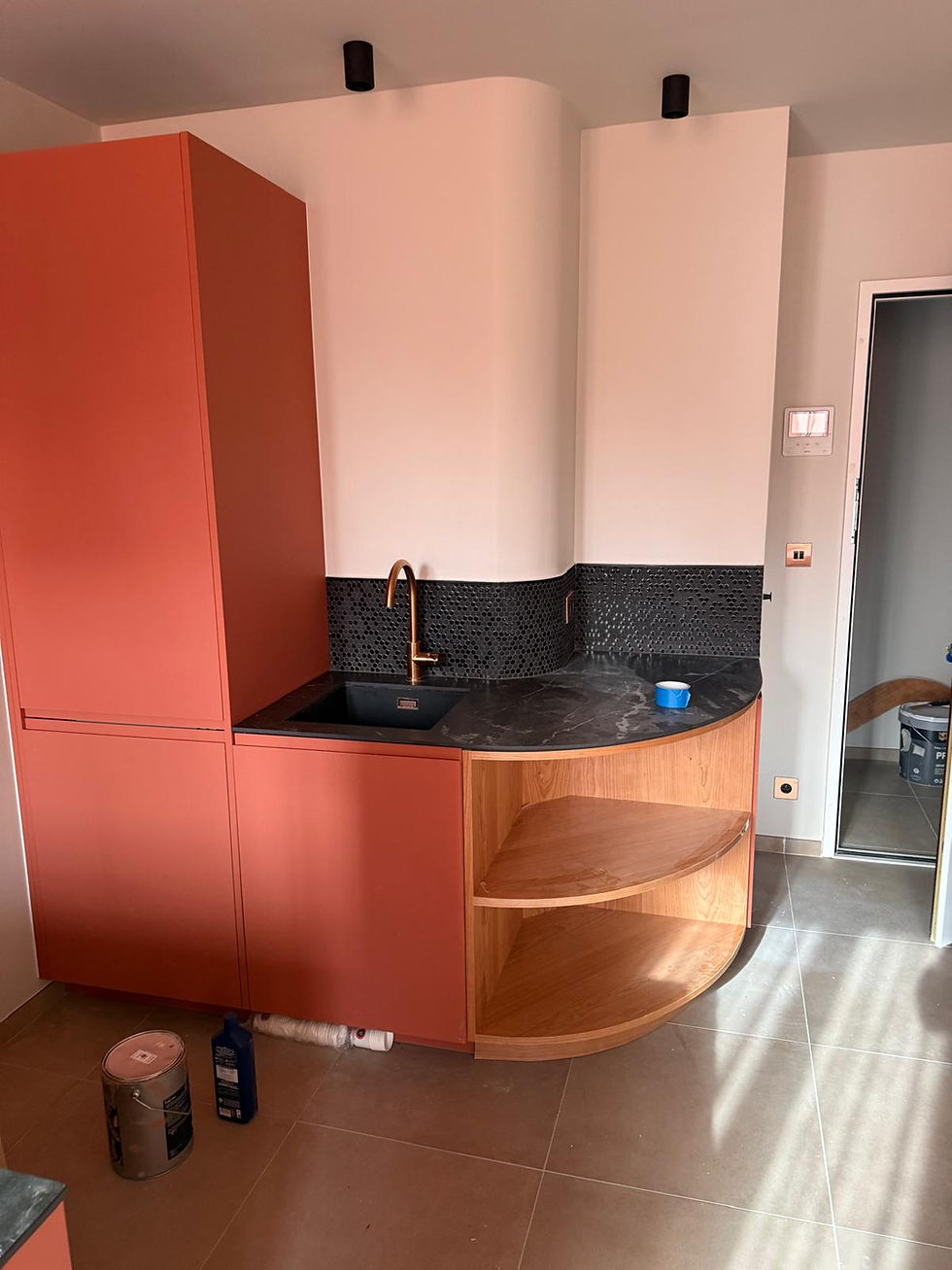 Un agencement sur-mesure en plaquage merisier est fixé aux caissons. La crédence en mosaïque noire est posée en épousant parfaitement l'arrondi du mur.