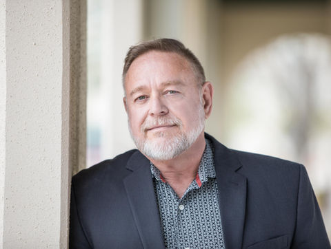 Headshot of a middle-age man leaning casually against a column while looking at the camera with confidence.