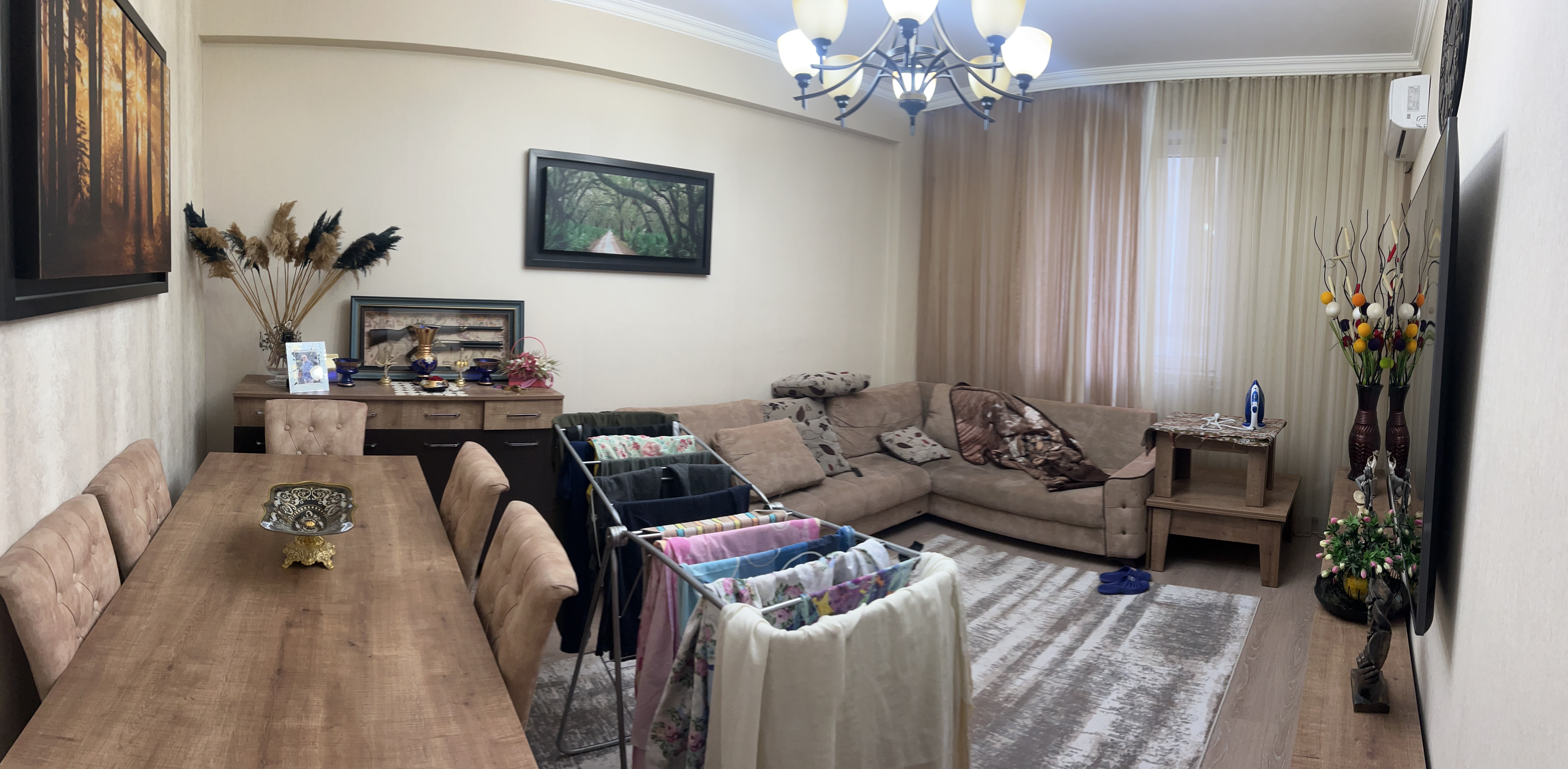 A cozy and stylish living room with bright blue and white traditional Greek island architecture visible through large windows. The interior features a modern orange and white sofa, elegant gold floor lamps, a wooden coffee table, and a bookshelf filled with books. Blue accents and Mediterranean elements create a warm, inviting atmosphere. This image was generated using ArchiVinci AI.