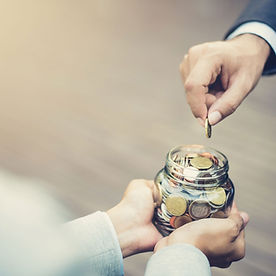 Someone's had dropping a coin into a glass jar full of coins held by two hands.