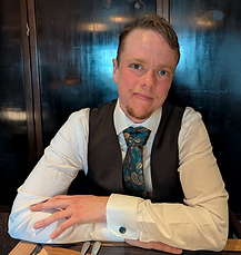 Silas Hooper, a white man with short hair and a beard, wearing a waistcoat and tie