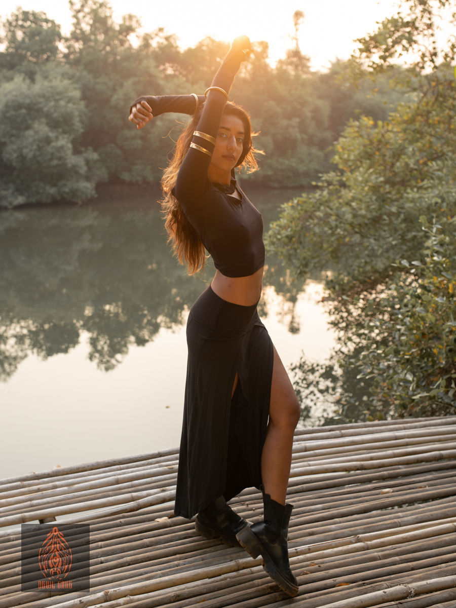 Thumbnail: Woman wearing black crop top and skirt, posing on wooden dock, water view.