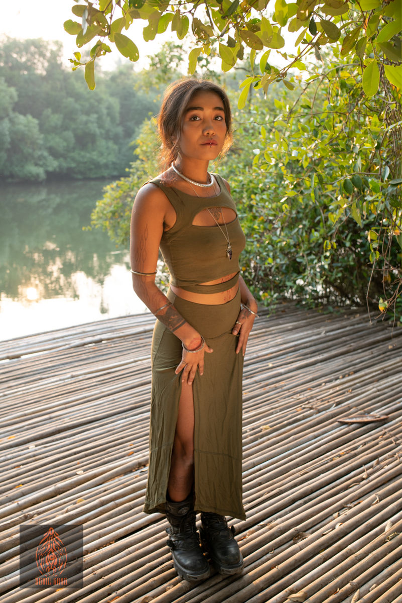 Thumbnail: Woman wearing olive green crop top and skirt, standing by water, Catana Clothing.