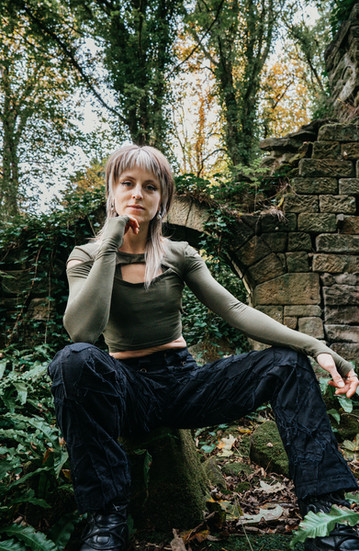 Woman sitting in front of stone wall, Catana Clothing, The Fall Cut, nature background.