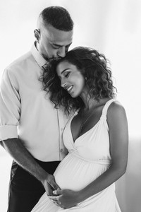 Couple maternity photoshoot in NYC studio with partner hugging from behind and hands on belly