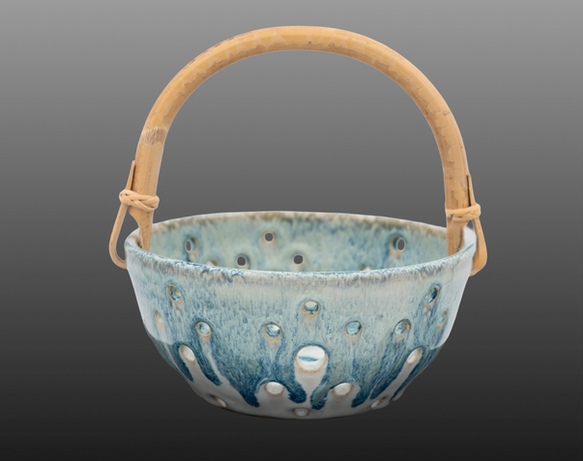 Blue ceramic berry basket with holes and a wooden handle. 