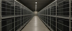 A row of industrial cages resembling factory farming enclosures, but containing computer servers instead of animals, symbolizing the large-scale instrumentalization and disposability of artificial minds.